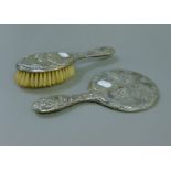 A silver dressing table mirror and a brush, each embossed with cherubs.