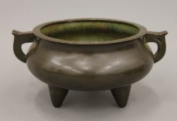A 19th century Chinese bronze circular twin handled censer of squat form on three short feet,
