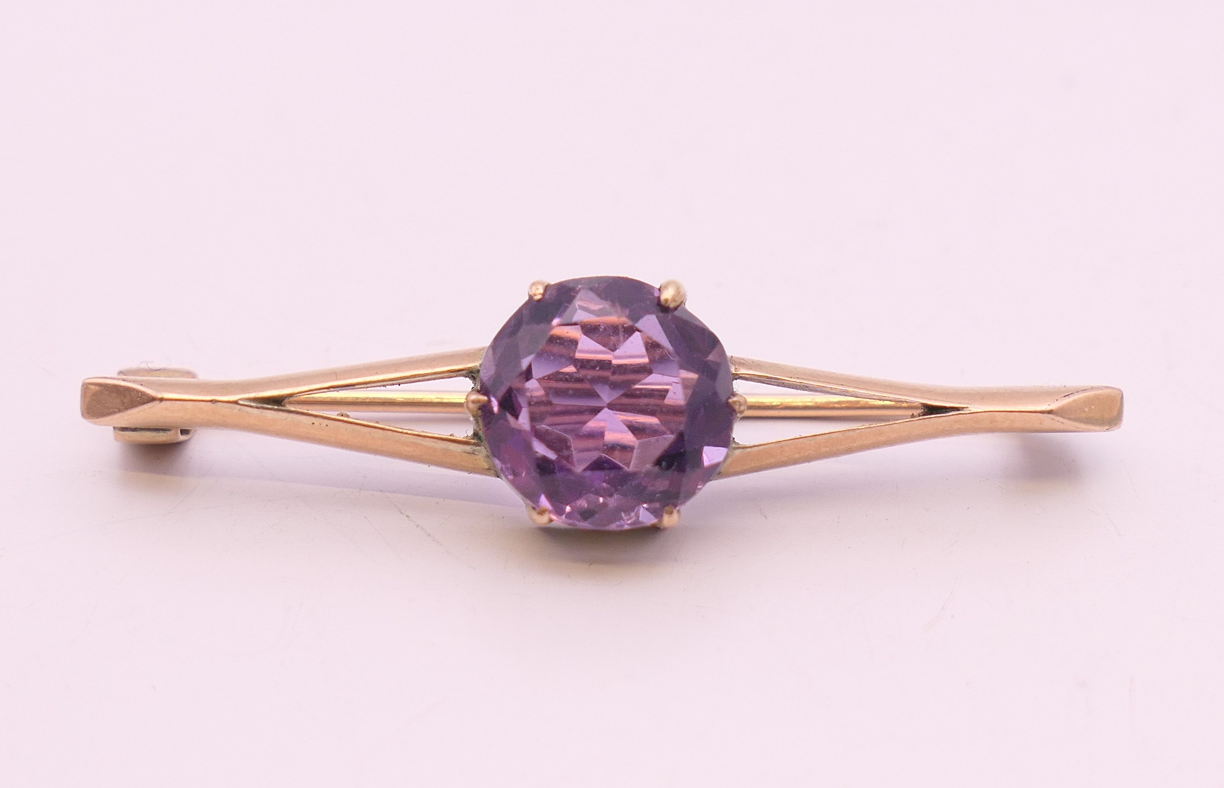 An unmarked 9 ct gold and amethyst bar brooch. 4 cm wide. 2.9 grammes total weight.