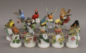 A quantity of various ceramic and glass bells decorated with bird form handles.