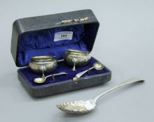 A boxed pair of silver salts and two salt spoons, and a silver berry spoon. The latter 22 cm long.