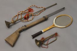 Two brass horns, a vintage tennis racket and a model gun.