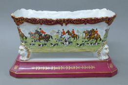 A porcelain jardiniere on stand decorated with hunt scenes. 35 cm wide.
