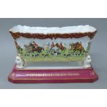 A porcelain jardiniere on stand decorated with hunt scenes. 35 cm wide.