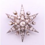 An unmarked gold diamond set star form pendant/brooch. 4 cm high. 10.7 grammes total weight.
