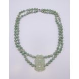 A green jade bead necklace with integral carved pendant on 14K white gold clasp. 64 cm long.