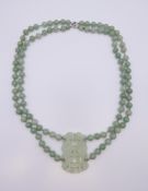 A green jade bead necklace with integral carved pendant on 14K white gold clasp. 64 cm long.