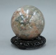 A Chinese marble specimen ball standing on a carved wooden plinth base. 16 cm high overall.