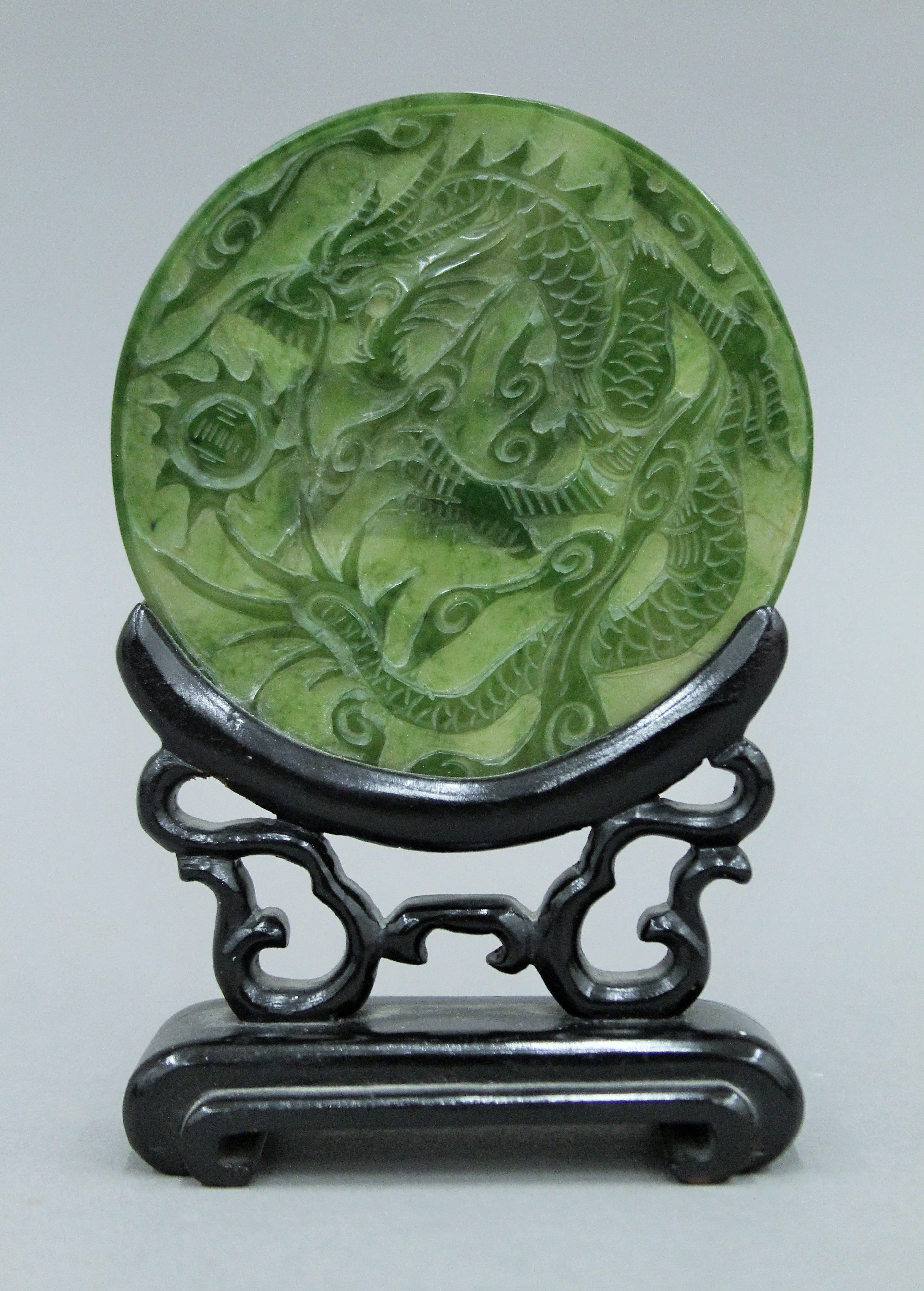 A small Chinese carved spinach jade disc on carved wooden stand. 13.5 cm high.