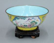 A late 19th/early 20th century Canton yellow ground enamel bowl on a wooden stand. 17 cm diameter.