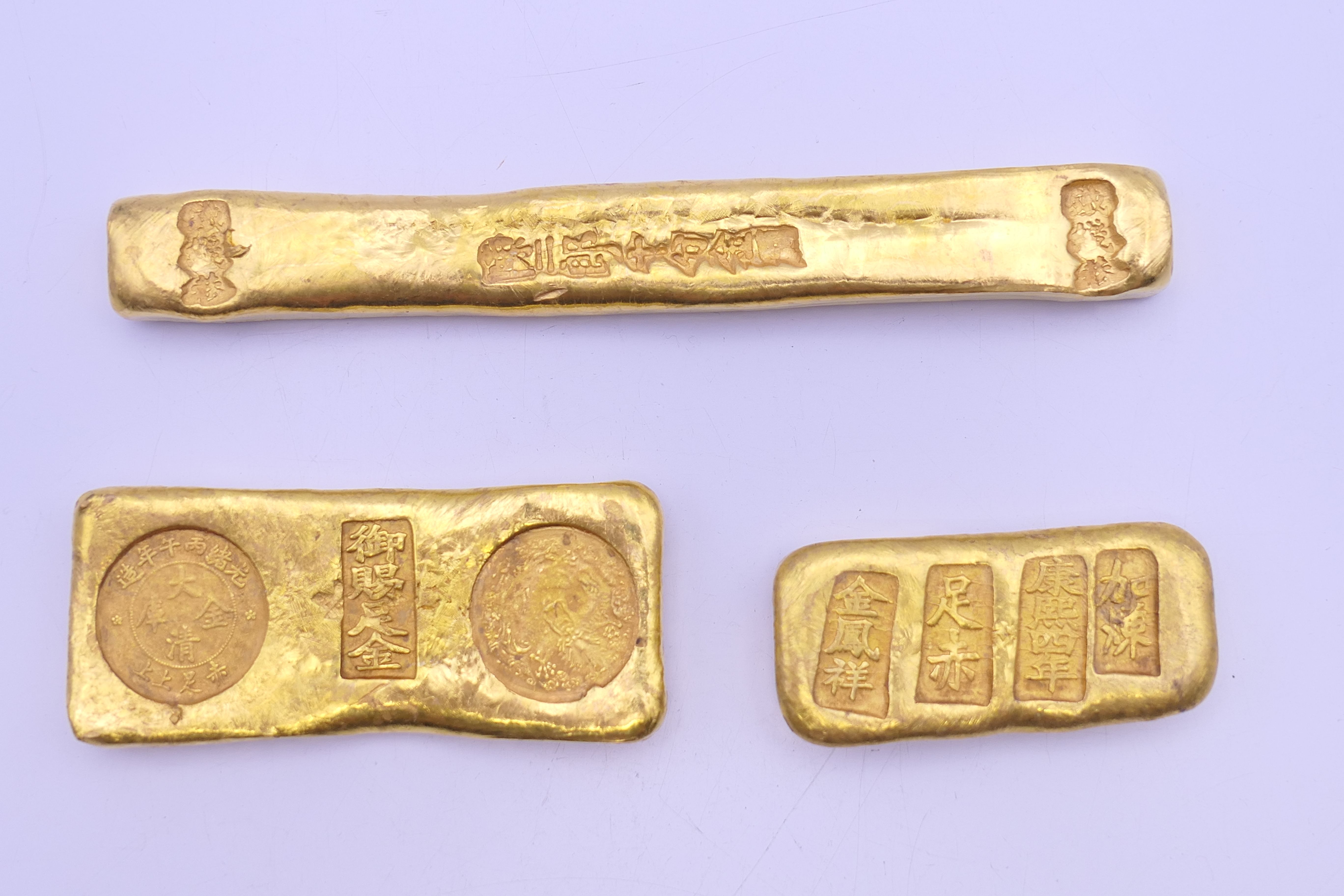 Three Chinese gold coloured bar scroll weights. The largest 12 cm long.