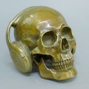 A bronze model of a skull wearing headphones. 18.5 cm wide.