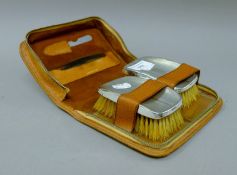A pair of silver back brushes in a pig skin travelling case. The case 19 cm wide.