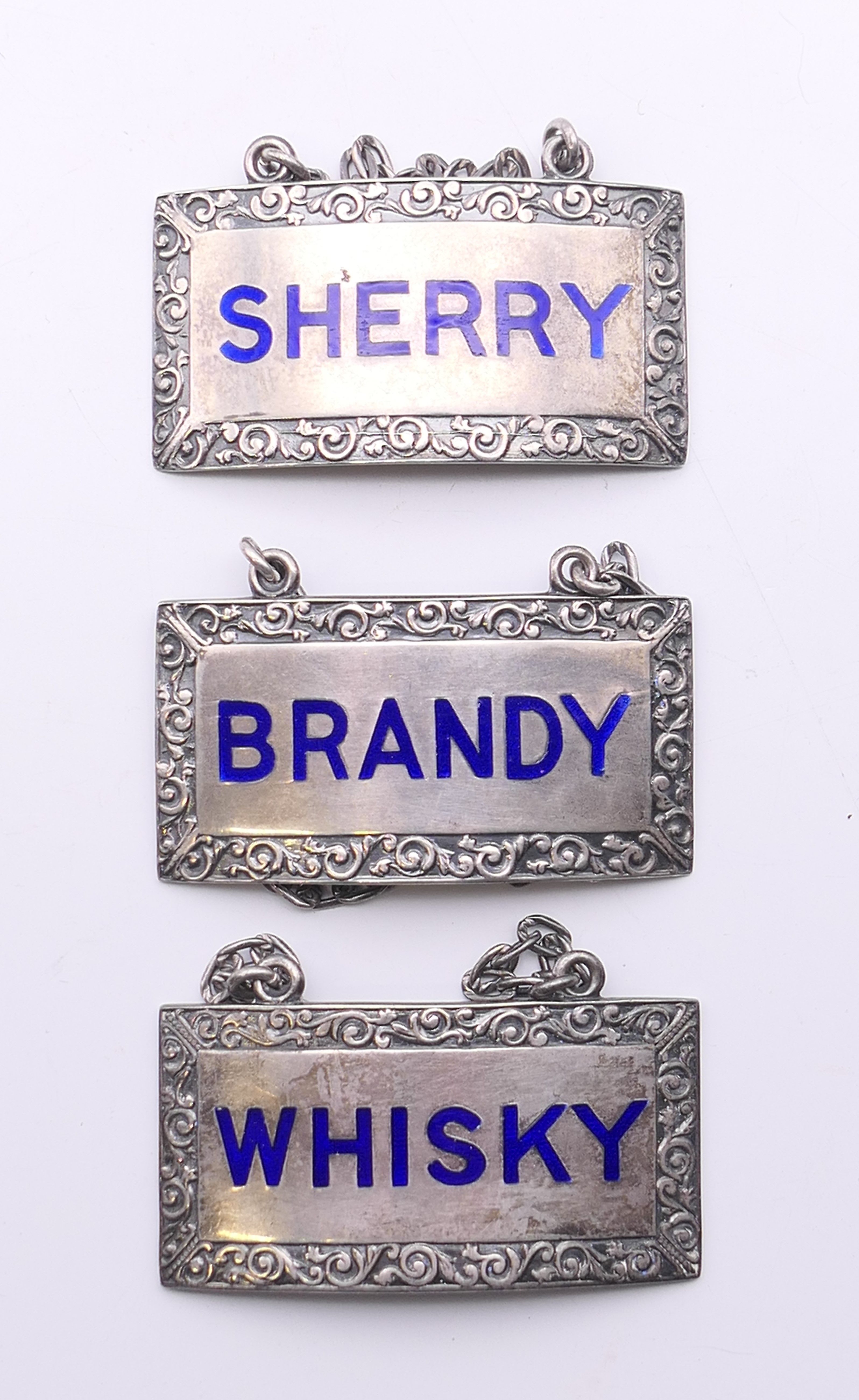 A set of three silver enamel decanter labels. 5 cm wide.