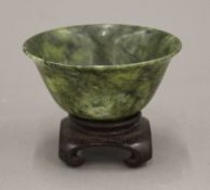 A Chinese green spinach jade bowl on wooden stand. 10 cm diameter.