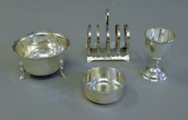 A silver toast rack, a silver egg cup and two small silver bowls. The former 7 cm long. 218.