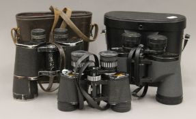 Three cased pairs of binoculars. The largest 20 cm high.