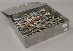 A quantity of medical instruments in a metal box. The box 31 cm wide.