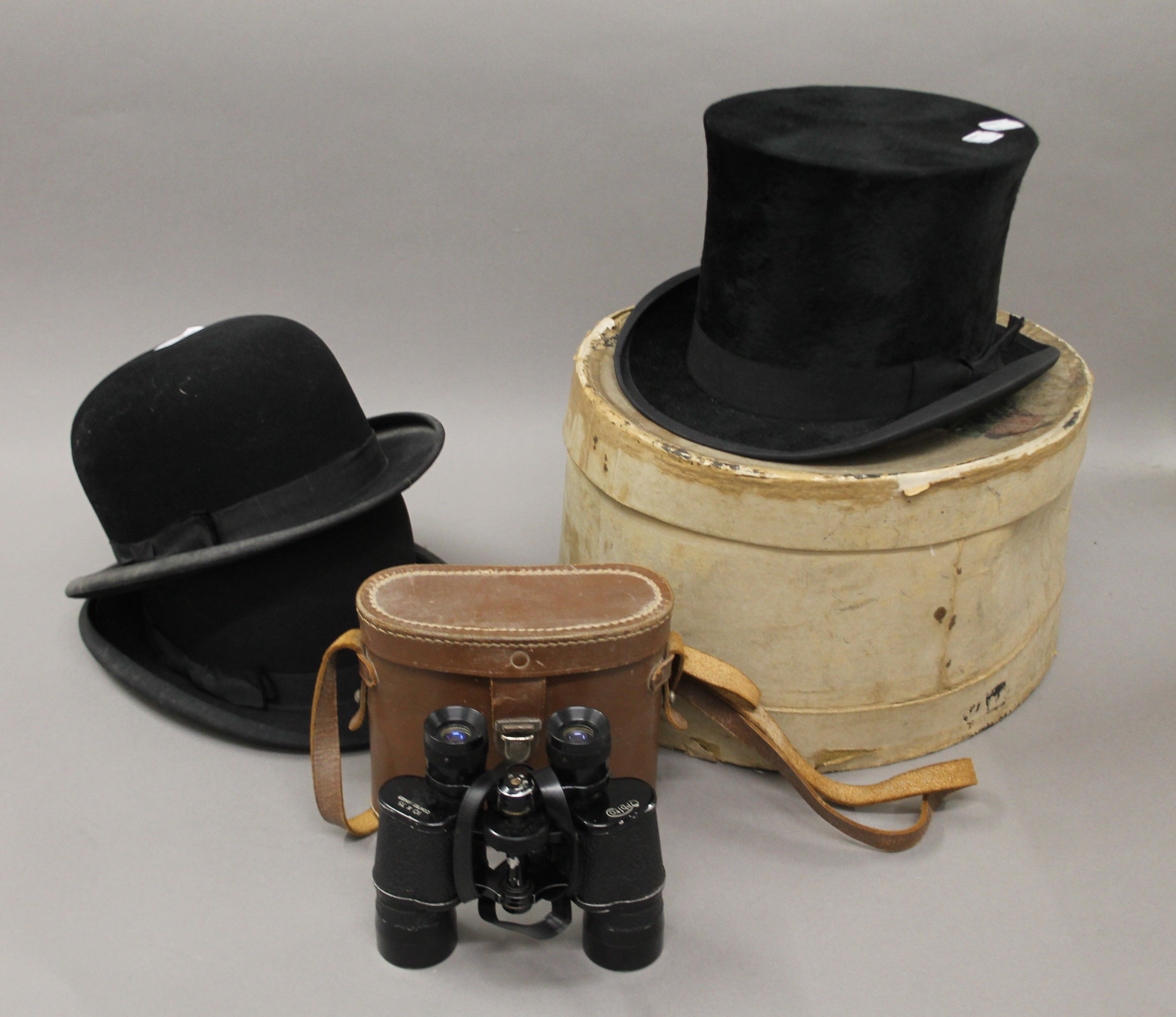 A boxed top hat, two bowler hats and a pair of binoculars.