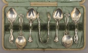 A cased set of Art Nouveau silver teaspoons and tongs. The case 54 cm wide. 112.4 grammes.