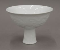 A Chinese white porcelain stem bowl, with moulded decoration of clouds and dragons,