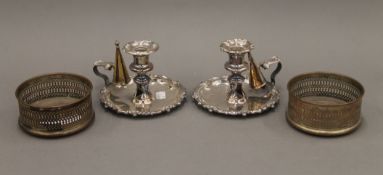 Two silver plated chambersticks and a pair of plated bottle coasters. The latter 12 cm diameter.