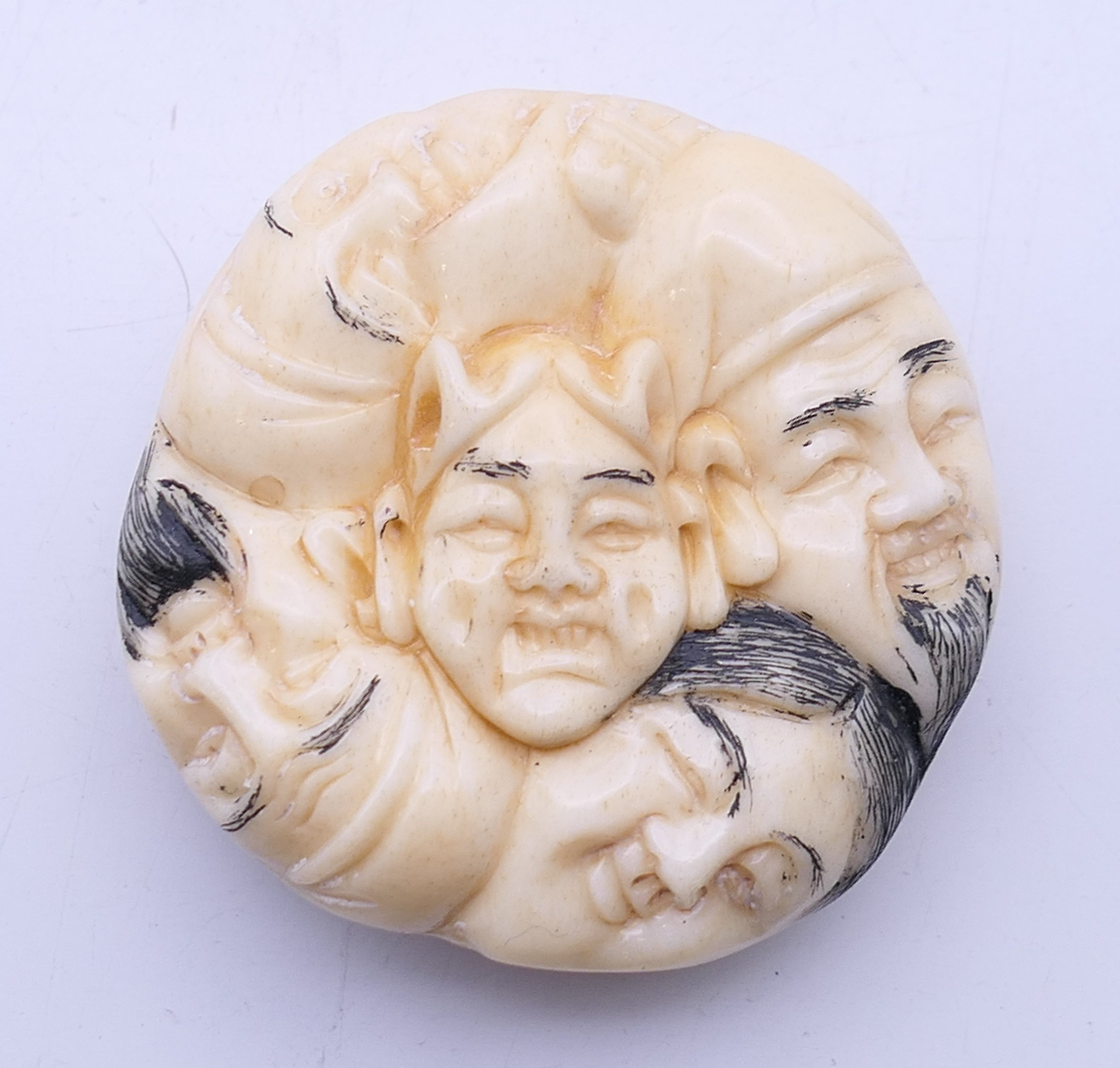 A bone carving of various faces. 4 cm diameter.