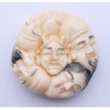 A bone carving of various faces. 4 cm diameter.