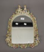 A large Continental porcelain florally encrusted mirror decorated with putti. 46.5 cm high.
