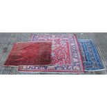 Two red ground wool rugs and a blue ground rug. The largest 180 cm x 134 cm.