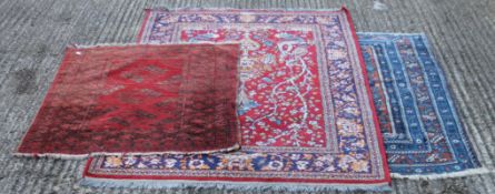 Two red ground wool rugs and a blue ground rug. The largest 180 cm x 134 cm.