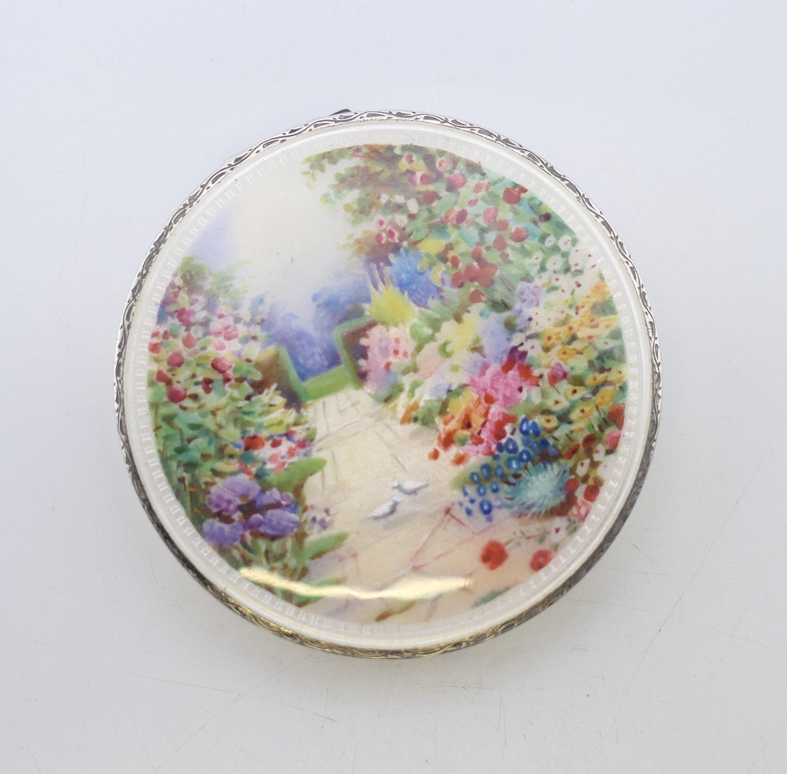 An early 20th century silver and enamel compact, the lid decorated with a floral garden scene. - Image 2 of 6