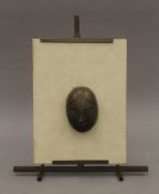 A bronze mask mounted on a small bronze easel. 32 cm high overall.