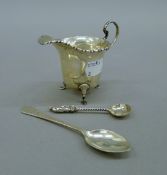A silver cream jug and two spoons. The former 7 cm high and 49.1 grammes.