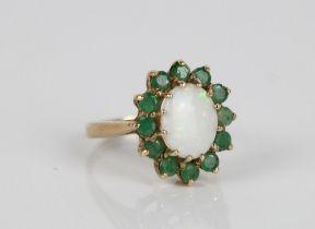 9ct gold opal and emerald cluster ring, the cabochon white opal surrounded by a halo of emeralds