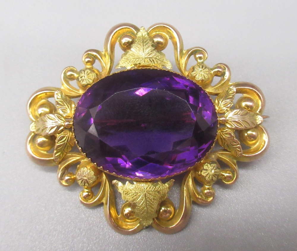 9ct yellow gold brooch set with large central oval cut amethyst, the border decorated with foliage