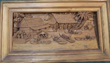 Large relief wooden carving of a market scene on a river bank with boats, huts and palm trees.