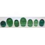 Group of seven green glass dumps, four with internal flowers, max H13cm.