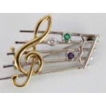 18ct yellow and white gold treble clef brooch, set with diamond, emerald and amethyst, stamped