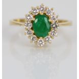 Yellow metal emerald and diamond cluster ring, the central oval cut emerald surrounded by a halo