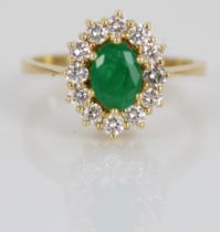 Yellow metal emerald and diamond cluster ring, the central oval cut emerald surrounded by a halo