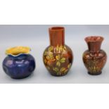 Two Linthorpe pottery brown glazed vases, decorated with flowers, and a blue glazed globular vase