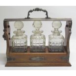 C19th or early C20th tantalus, with three cut glass decanters mounted in an oak and silver plate