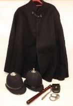 Police uniform items comprising woollen cape, two helmets, truncheon, and a pair of handcuffs marked