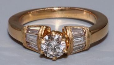 Yellow metal diamond ring, the central brilliant cut diamond in claw settings on tapered baguette