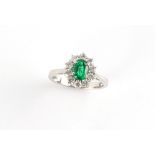 A platinum emerald & diamond oval cluster ring, the oval cut emerald of vibrant colour and