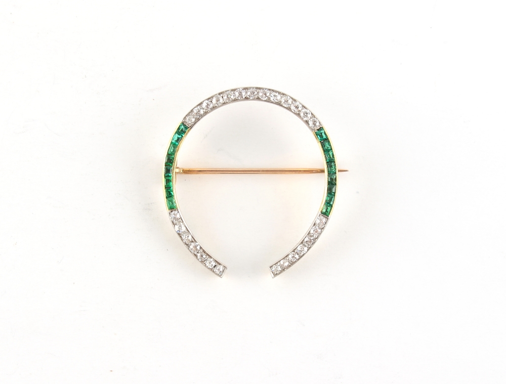 An unmarked yellow gold emerald & diamond horseshoe brooch, set with calibre cut emeralds & round