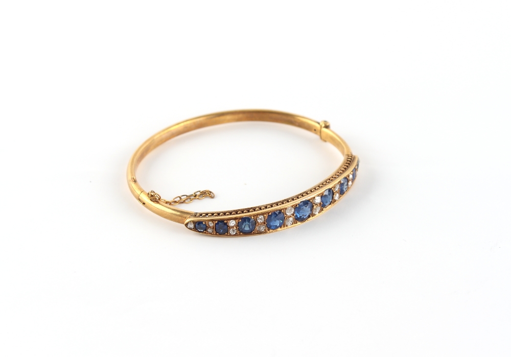A late Victorian yellow gold (tests 15ct) sapphire & diamond hinged bangle, the nine well matched