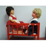 A Pedigree Walking Doll, together with one other doll, in a red cot.