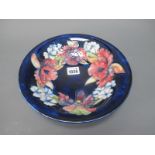 A Moorcroft Pottery Shallow Circular Bowl, painted with the 'Orchid' pattern against a dark blue